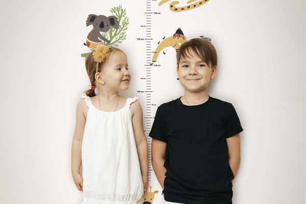 Brother and sister measuring their height near home wall